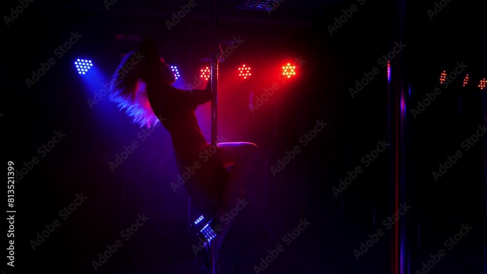 A flexible dancer performs a complex exercise on a pylon in the dark with the light of green, red and blue projectors. Pole dance. Slow motion. Silhouette. A flexible dancer performs a complex exercise on a pylon in the dark with the light of green, red and blue projectors. Pole dance. Slow motion. Silhouette.
