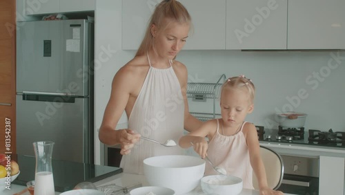 A woman and a toddler are happily cooking in a blond homemakers kitchen photo
