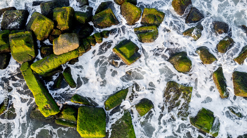 Aerial view of coastal defenses with moss-covered tetrapods and groynes against eroding waves, suitable for environmental studies and World Oceans Day photo