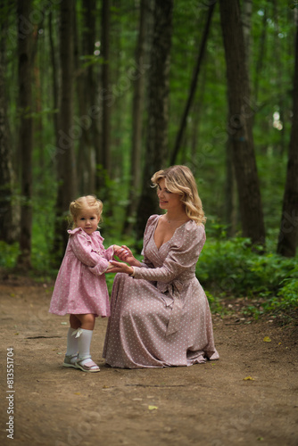 Mother gently holds her daughter in the woods, finger to lips for quiet. Captures a moment of teaching and gentle guidance.