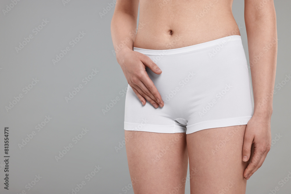 Woman holding hand near panties on grey background, space for text. Women's health