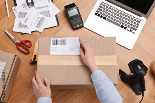 Parcel packing. Post office worker sticking barcode on box at wooden table, top view