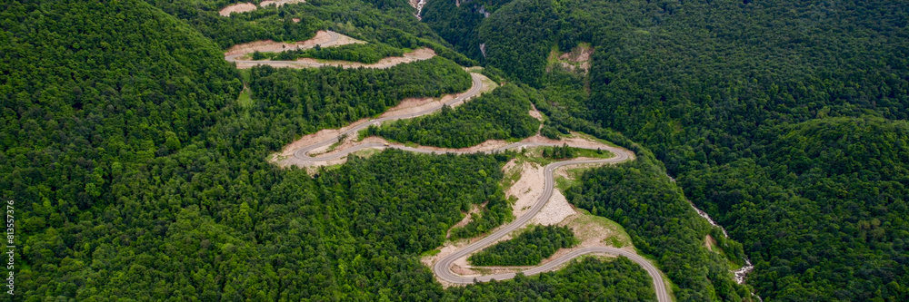 Aerial view of a winding road snaking through a lush green forest, conceptually ideal for travel, adventure, and environmental themes Aerial view of a winding road snaking through a lush green forest, conceptually ideal for travel, adventure, and environmental themes