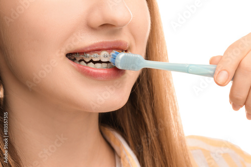 Smiling woman with dental braces cleaning teeth on white background  closeup