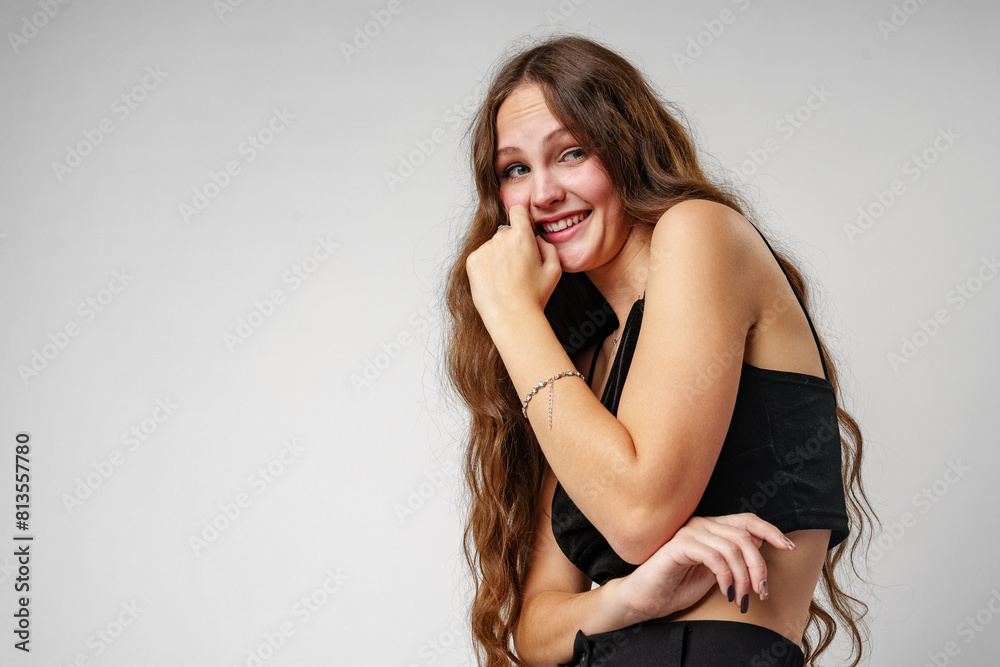 Fototapeta premium Smiling Young Woman Posing in a Black Top Against a Grey Background