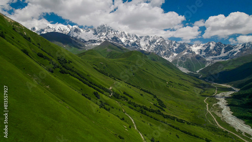 Breathtaking panoramic view of vibrant green meadows leading to snow-capped peaks under a blue sky, ideal for nature and travel themes, Earth Day promotions