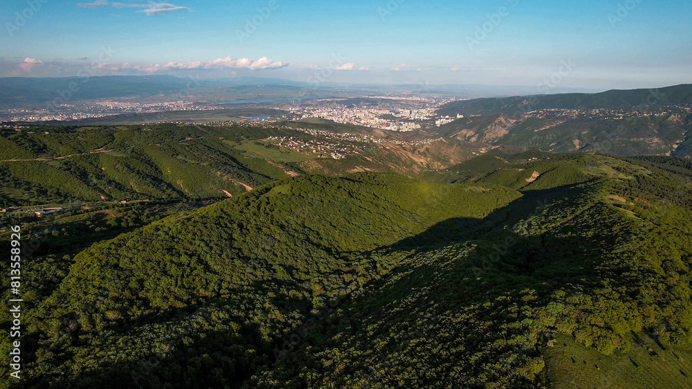 Fototapeta premium Aerial view of a majestic green canyon with winding trails under the blue sky, ideal for nature backgrounds and Earth Day promotions