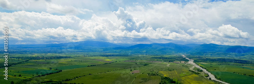 Panoramic view of a serene valley with a meandering river  green fields  and distant mountains under a cloudy sky  suitable for Earth Day and World Environment Day concepts