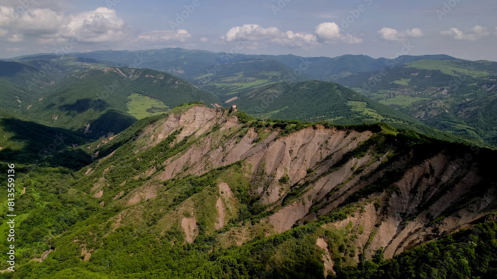 Naklejka premium Breathtaking aerial view of a majestic green mountain range with unique rock formations under a clear sky, ideal for nature and travel themes