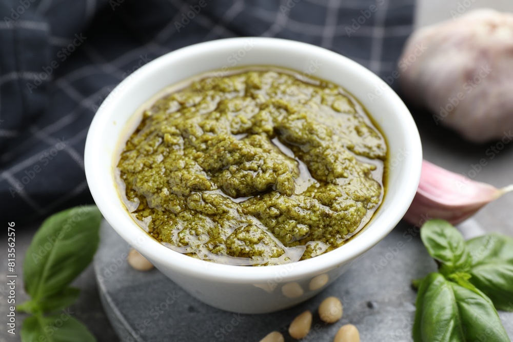 Tasty pesto sauce in bowl, basil, pine nuts and garlic on table, closeup Tasty pesto sauce in bowl, basil, pine nuts and garlic on table, closeup