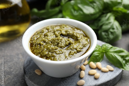 Tasty pesto sauce in bowl, basil and pine nuts on grey table, closeup