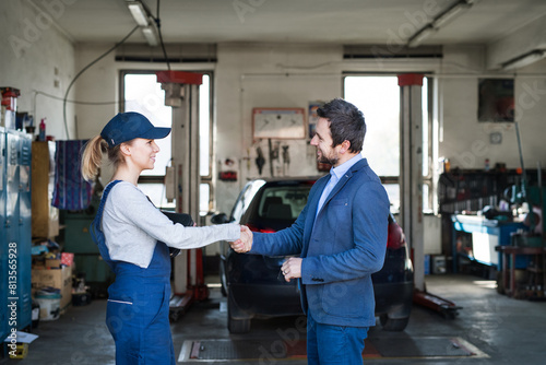 Female auto mechanic talking with customer  shaking hands. Beautiful woman working in a garage  wearing blue coveralls.