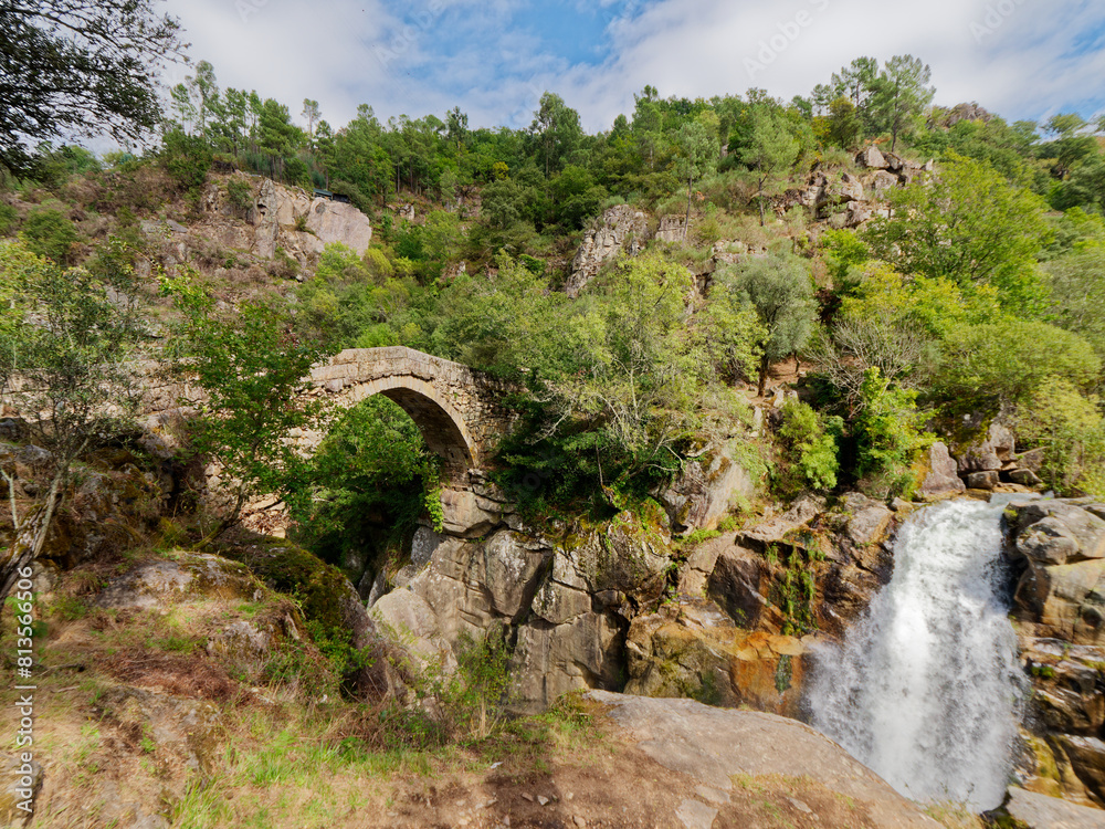Ponte da Misarela or Bridge of Mizarela in Montalegre, Portugal with a big waterfall next to it during a sunny day. Rural travel and holidays in nature.