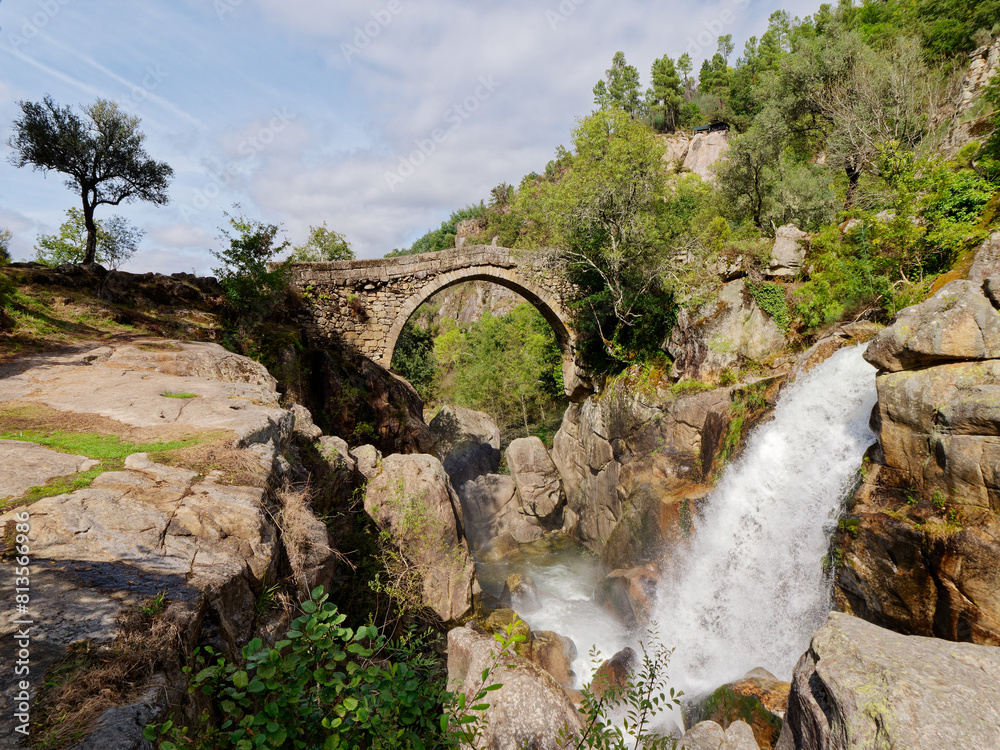 Ponte da Misarela or Bridge of Mizarela in Montalegre, Portugal with a big waterfall next to it during a sunny day. Rural travel and holidays in nature.