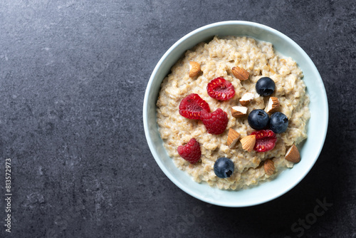 Oatmeal porridge with raspberries, blueberries and  almonds in bowl on black background. Top view. Copy space