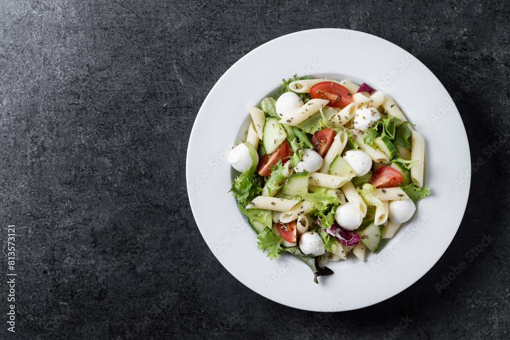 Pasta salad with vegetables and mozzarella cheese on black background. Top view. Copy space Pasta salad with vegetables and mozzarella cheese on black background. Top view. Copy space