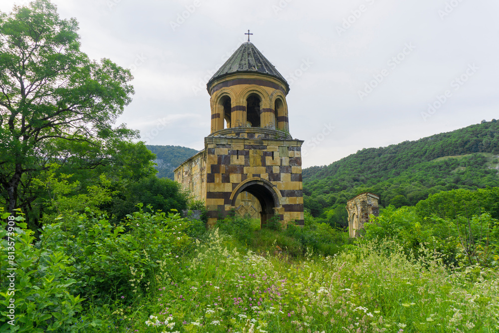 The medieval bell tower is built of multi-colored stones. Cross on the roof