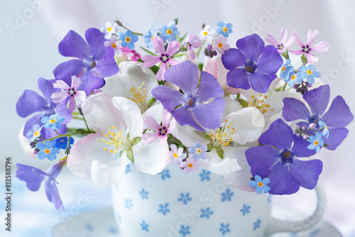 Bouquet of spring flowers in a cup, periwinkle, forget-me-nots, blooming apple tree, phlox. Closeup, blur, beautiful postcard.