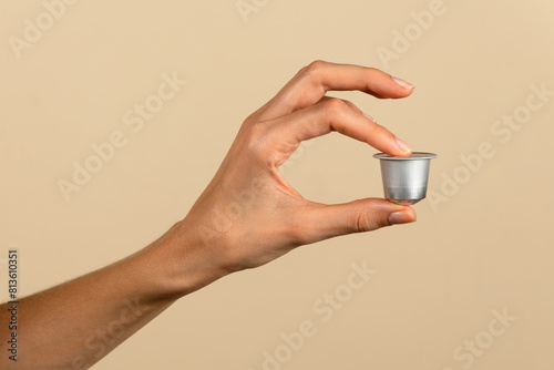 Hand holding coffee capsule on neutral background