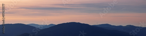 Banner 4x1 Linkedin. Black silhouettes of alpine mountains with windmills on peaks at sunset