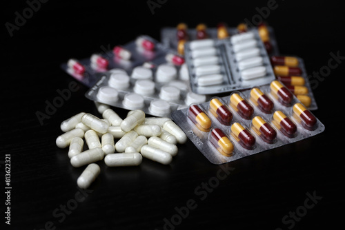 Pills on a black wooden table, variation of scattered medication in capsules. Background for pharmacy, antibiotics, vitamins