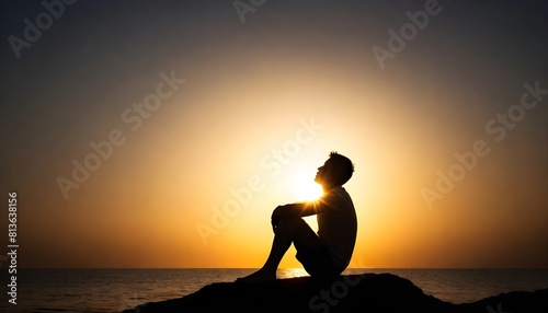 A silhouette of a man sitting on a rock against the backdrop of a setting sun, casting long shadows © Sema