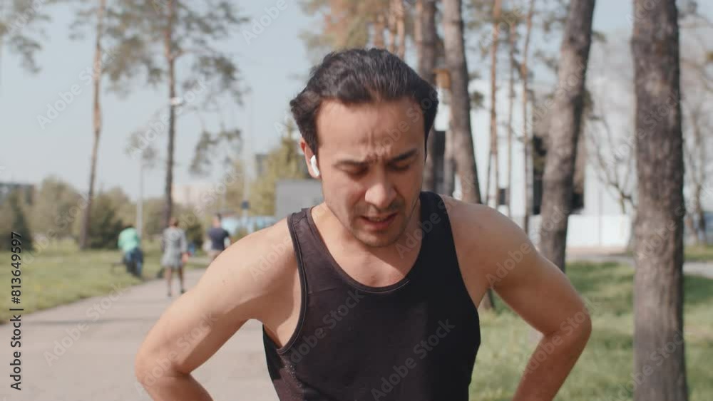 Young asian male jogger walking down the alley in an autumn city park during pause in the workout and turn on music on the headphones, front view. Concept of modern outdoor sports training in a casual Young asian male jogger walking down the alley in an autumn city park during pause in the workout and turn on music on the headphones, front view. Concept of modern outdoor sports training in a casual