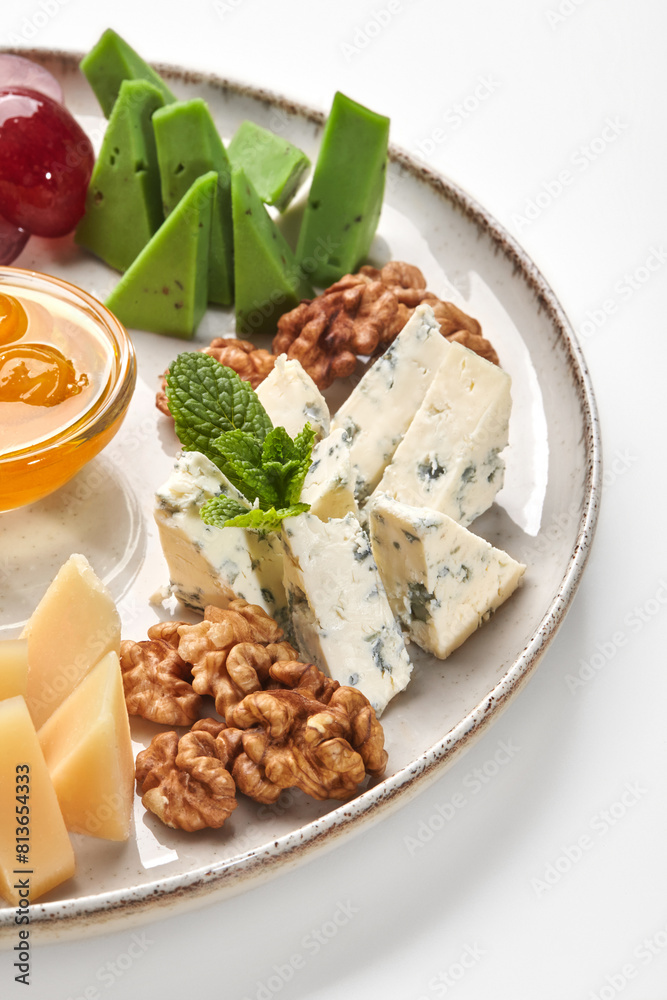 Ceramic plate with variety of cheeses, honey, grapes and walnut