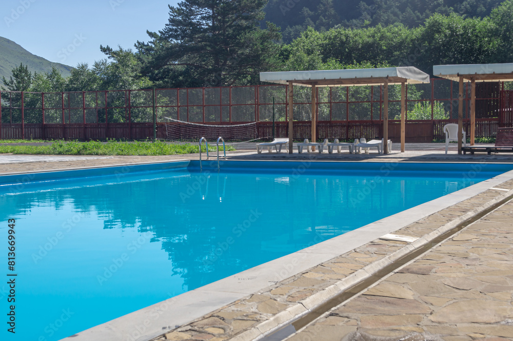 A heated pool high in the mountains. Relaxing by the water in the fresh air. Sun loungers for relaxing and sunbathing near the blue water pool. Vacation in the mountains in summer.