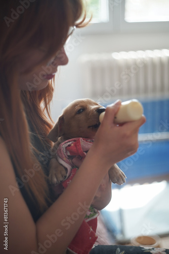 Young redhead woman feeding pet dog puppy with a milk bottle 
