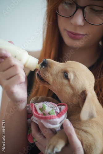 Young redhead woman feeding pet dog puppy with a milk bottle 