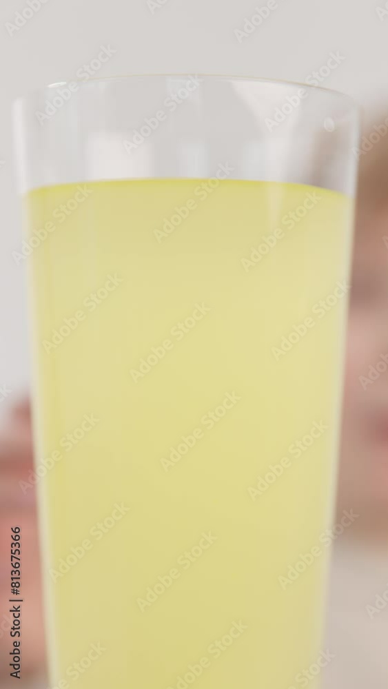 Vertical video. The silhouette of a blurred boy takes a glass of lemon and lime juice with two hands, close-up. The concept of natural lemonade for children's health. Vertical video. The silhouette of a blurred boy takes a glass of lemon and lime juice with two hands, close-up. The concept of natural lemonade for children's health.