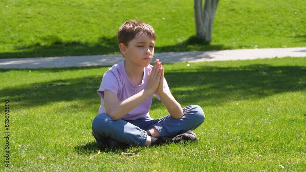 boy child sitting on green grass. child folded arms looking at the sun, the sky. child praying. child dreaming boy child sitting on green grass. child folded arms looking at the sun, the sky. child praying. child dreaming