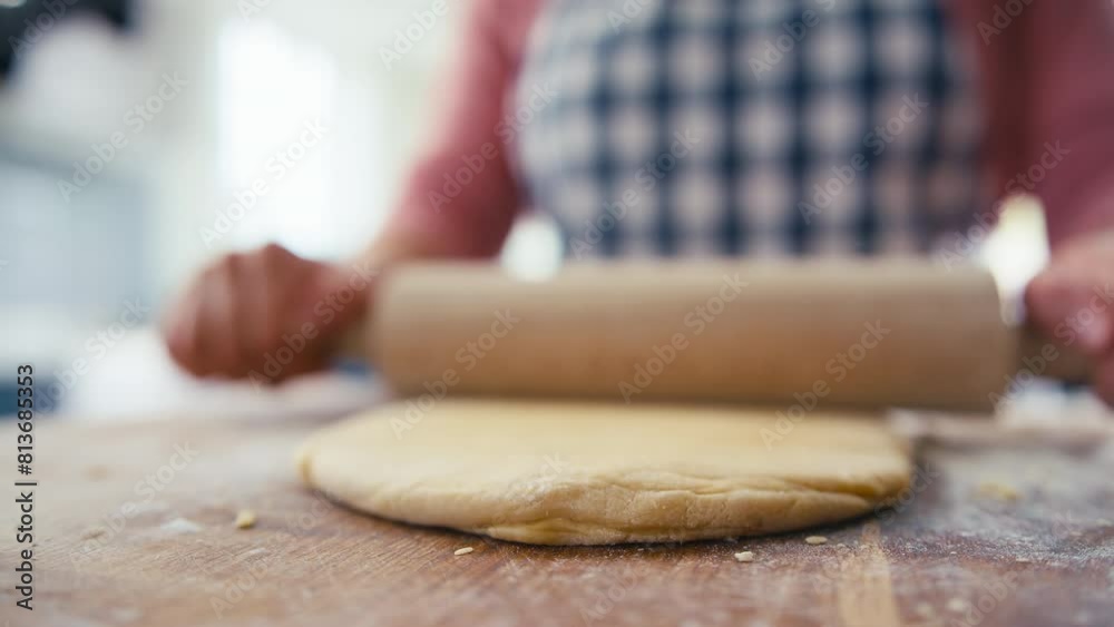 Close up of woman in kitchen rolling out dough with rolling pin on wooden board to make pasta - shot in slow motion