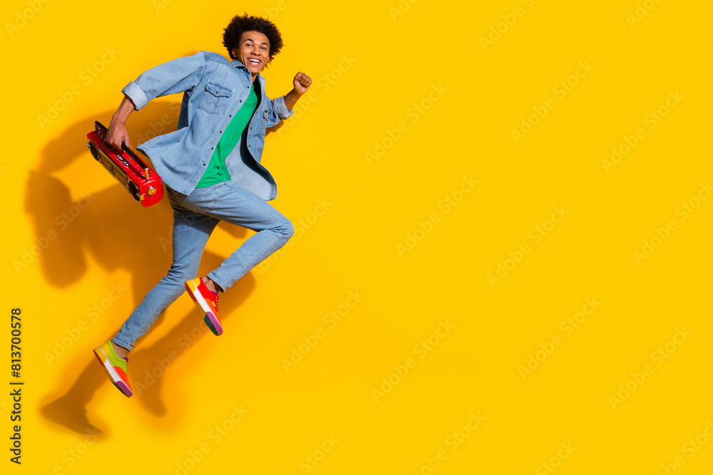Full size portrait of nice young man boombox run jump empty space wear denim shirt isolated on yellow color background