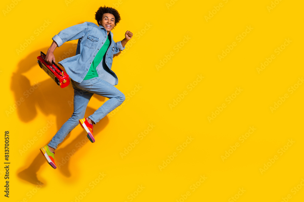 Full size portrait of nice young man boombox run jump empty space wear denim shirt isolated on yellow color background Full size portrait of nice young man boombox run jump empty space wear denim shirt isolated on yellow color background