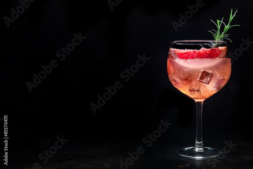 Fancy cocktail with fresh fruit. Gin and tonic drink with ice at a party, on a black background. Alcohol with pink grapefruit and rosemary, with a place for text