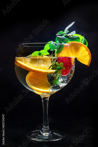 Cocktail with fresh fruit. Gin and tonic drink with ice at a party, on a black background. Alcohol with orange, mint, and strawberry
