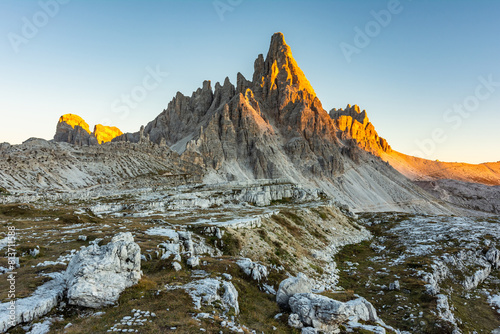 Monte Paterno mountain illuminated by a brilliant golden sun at golden hour sunset in early autumn on a bright sunny day next to the Dolomite landmark Tre Cime di Lavaredo