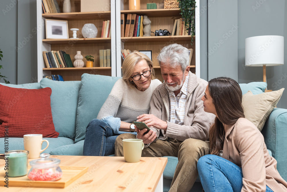 Simple living. Daughter visited her senior parents at home, looking at family photos on smartphone, evoting memories. Older man and woman happy that their daughter came to visit. Simple living. Daughter visited her senior parents at home, looking at family photos on smartphone, evoting memories. Older man and woman happy that their daughter came to visit.