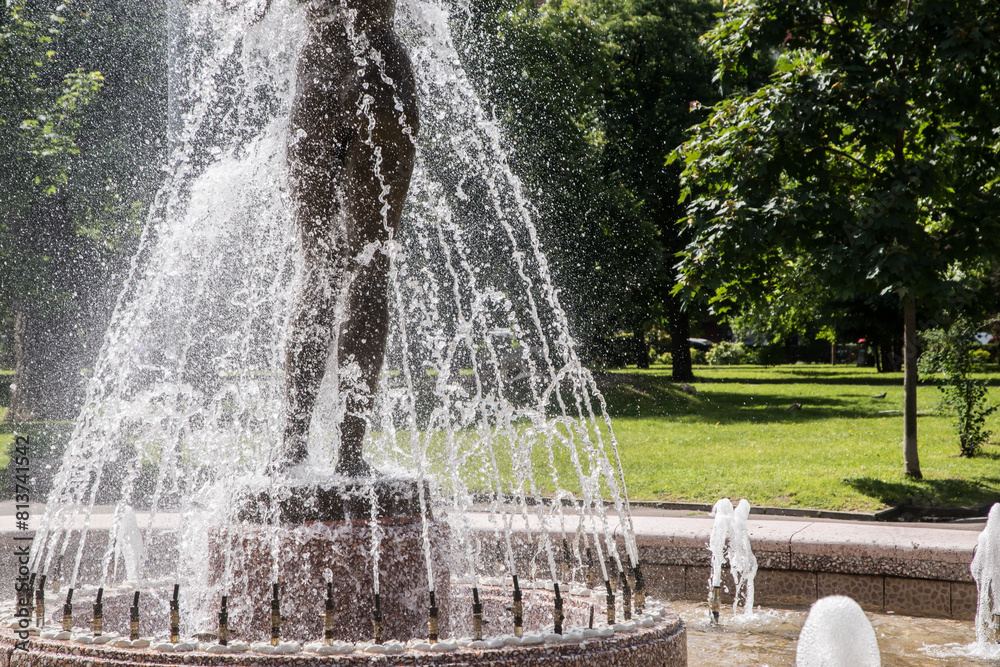 Naklejka premium Fountain in city park on sunny summer day with water splashes