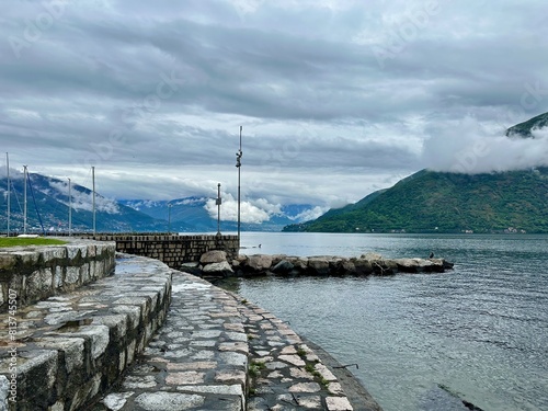 Tableau sur toile Serene Lakeside View in Cannobio, Featuring Cloud-Covered Mountains and a Stone