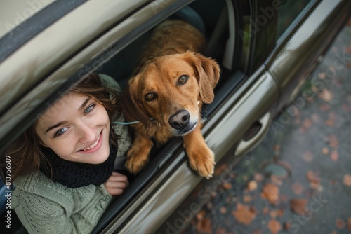 A young woman sits in the drivers seat of a car, smiling, with a dog beside her, both looking out of the window