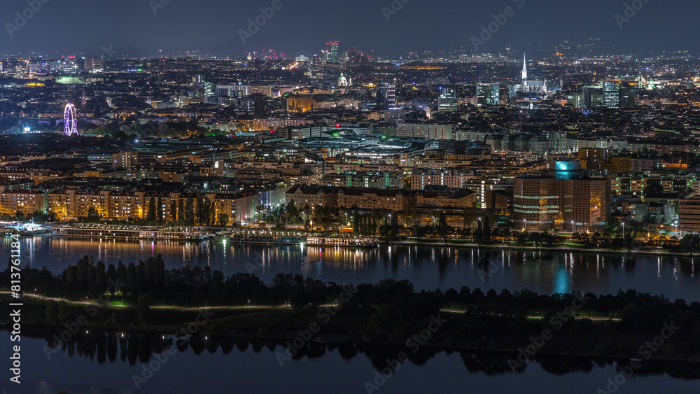 Fototapeta premium Aerial panoramic view over Vienna city with skyscrapers, historic buildings and a riverside promenade night timelapse in Austria.
