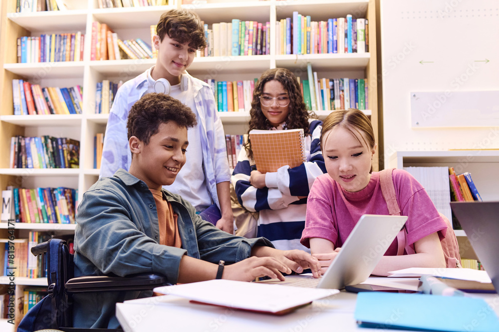 Portrait of smiling teenage boy using laptop in school library with diverse group of students working on project together