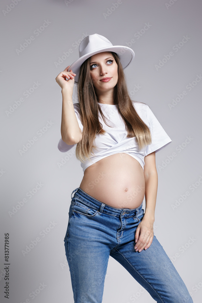 Young pretty pregnant woman in white t-shirt, hat and jeans. Female with belly exposed. 5th month of pregnancy Young pretty pregnant woman in white t-shirt, hat and jeans. Female with belly exposed. 5th month of pregnancy
