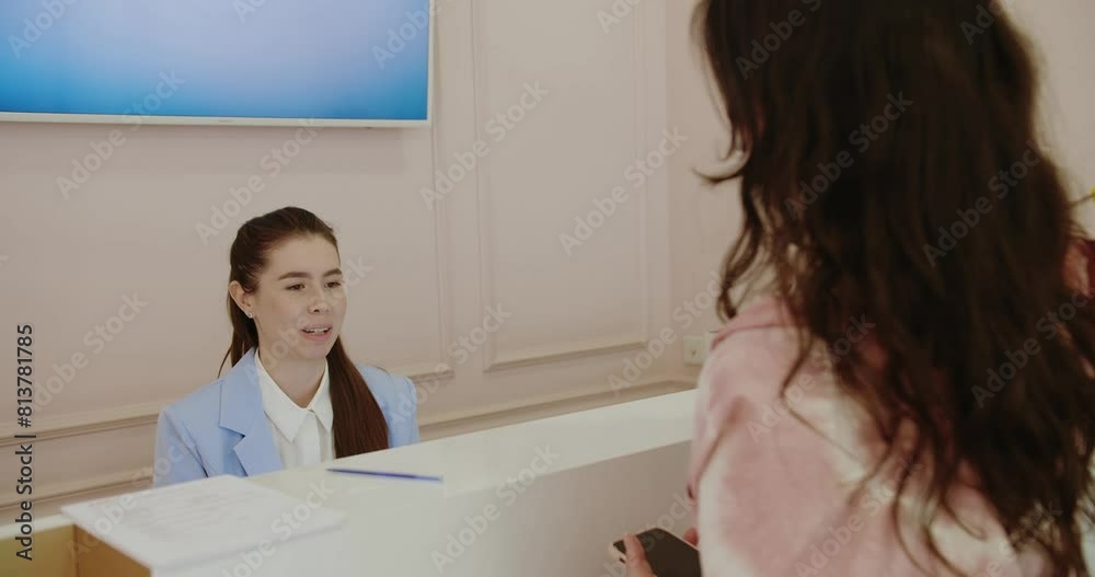 A friendly female receptionist at a healthcare clinic assists a female client. The reception area is clean and professional. Friendly Receptionist Assisting Client at Modern Health Clinic A friendly female receptionist at a healthcare clinic assists a female client. The reception area is clean and professional. Friendly Receptionist Assisting Client at Modern Health Clinic