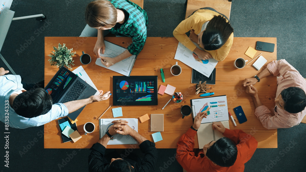 © Summit Art Creations - Top view of smart business man standing while writing and presenting marketing idea at whiteboard. Group of diverse happy people looking at stock market chart and listening presentation. Convocation.
