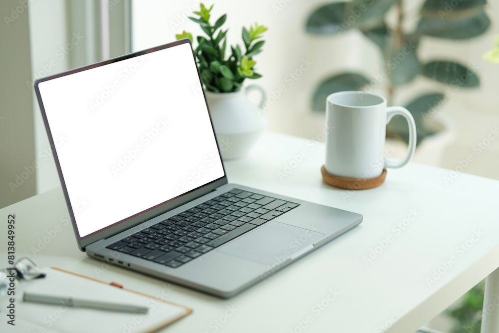 Laptop with blank display, glasses, notebook and houseplant on wooden table near glass window. Laptop with blank display, glasses, notebook and houseplant on wooden table near glass window.