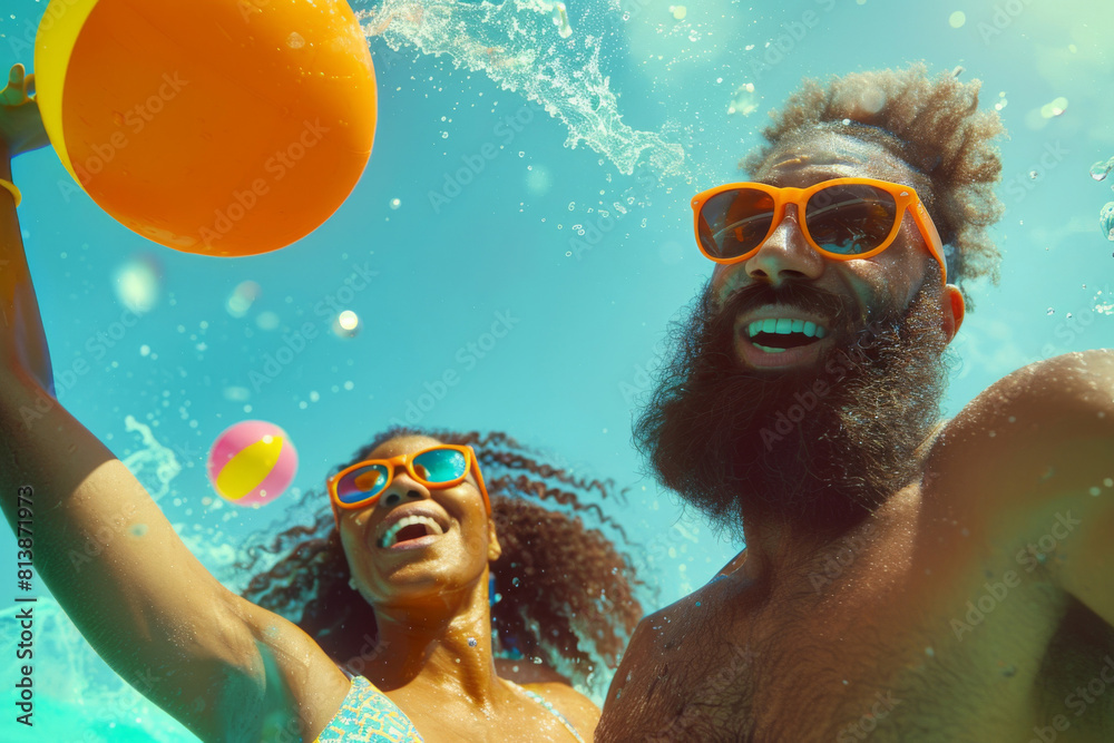 Underwater view of a happy couple having fun with a ball in a sunny swimming pool, wearing bright orange sunglasses